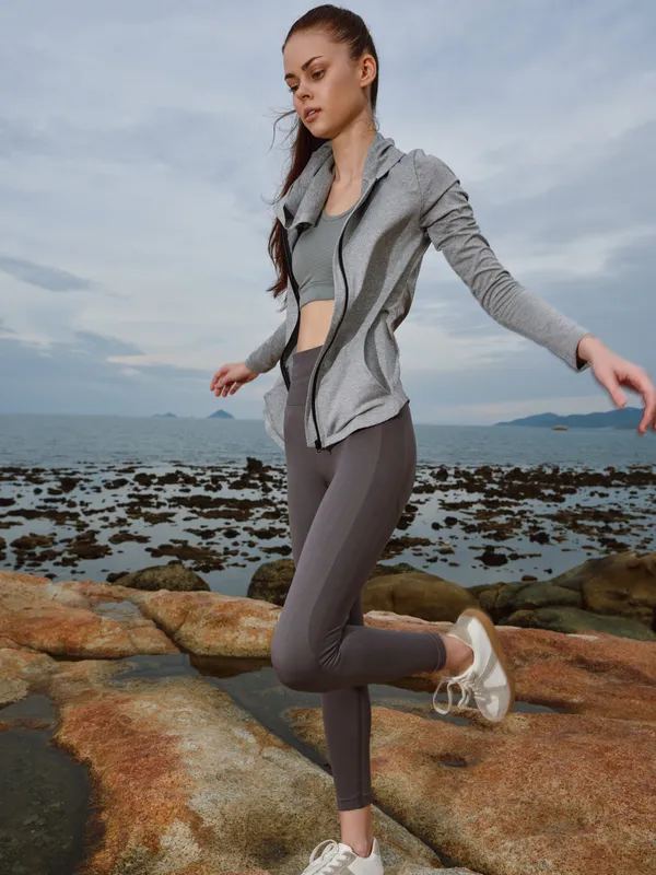 Young athletic woman in sportswear performing a fitness pose by the seaside, showcasing vitality and energy against a stunning natural background