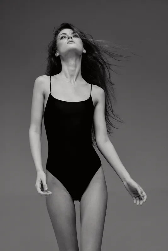 Black and white portrait of a young woman in a black swimsuit with flowing hair and a confident pose