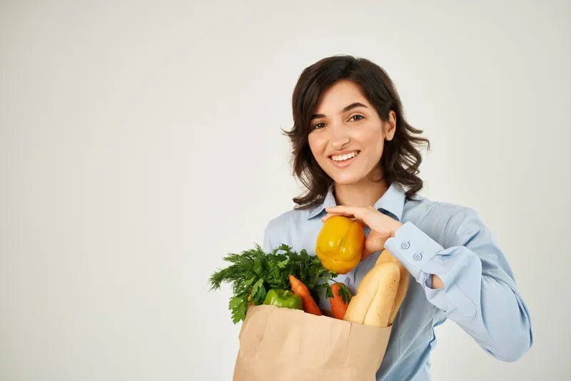 Женщина в голубой рубашке с пакетом продуктов, здоровой едой на светлом фоне
