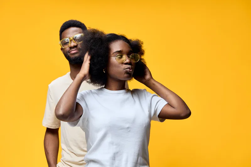 Stylish young couple with afro hairstyle wearing sunglasses against a vibrant yellow background, emphasizing a trendy and playful vibe in a summer setting
