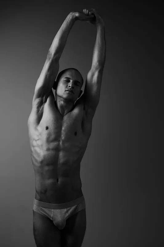 A muscular man stretching in a dramatic black and white setting, showcasing strength and elegance in motion. Perfect for fitness and wellness themes.
