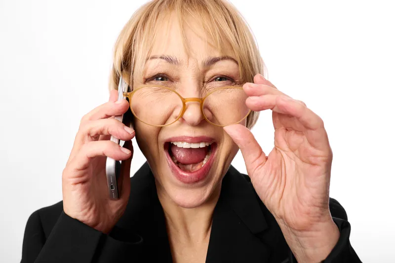 Senior woman with glasses laughing while talking on a mobile phone against a clean white background joyful business communication portrait concept for happiness