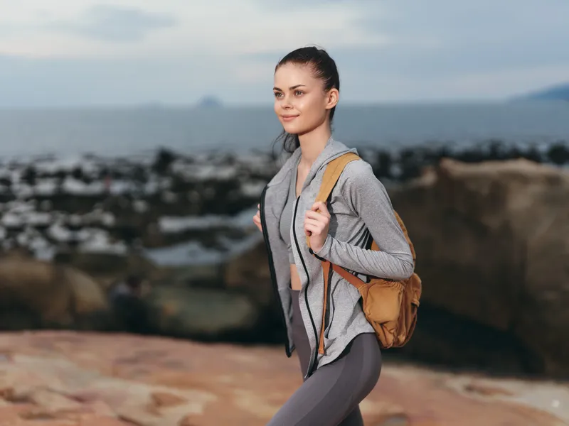 Young woman hiking on rocky beach, wearing active sportswear, smiling and enjoying nature, embodying healthy lifestyle and outdoor adventure
