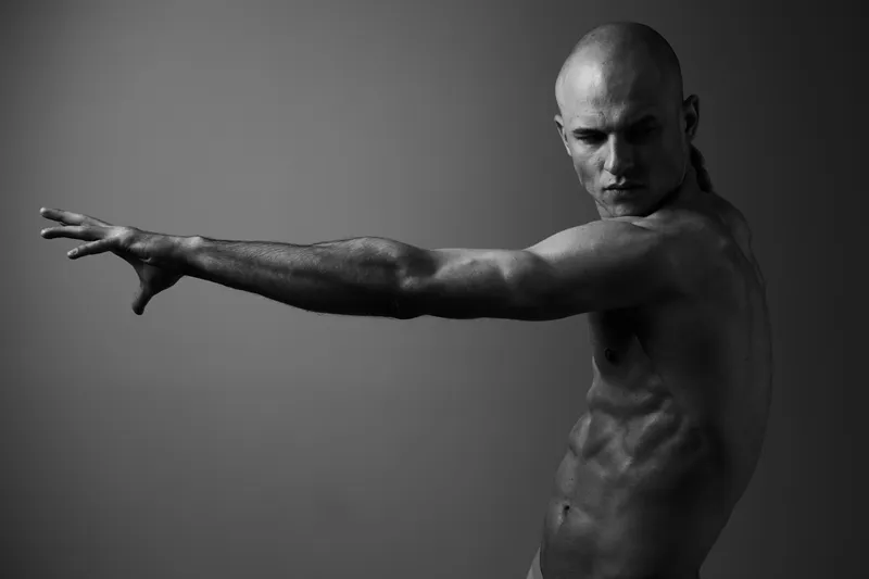 Strong man posing dynamically in a black and white image, showcasing his muscular physique and intense expression, emphasizing strength and determination.