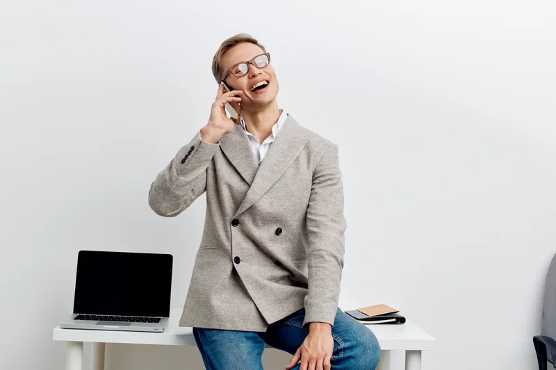 Smiling woman doctor talking on mobile phone while sitting at desk in office, casual professional attire, glasses, modern workspace with laptop and documents, cheerful mood, bright lighting, professio