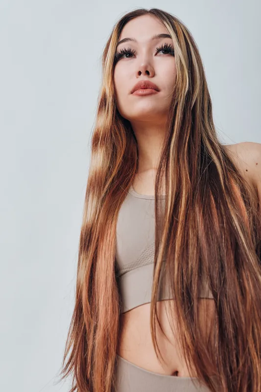 Young woman with long straight hair posing in beige sportswear on light background, beauty and confidence in casual comfortable outfit for lifestyle concept.