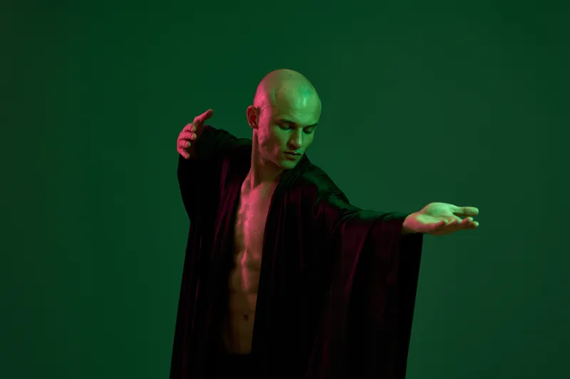 A man in a flowing black robe strikes a graceful pose, showcasing movement and elegance against a green backdrop. This captivating image is ideal for artistic themes.