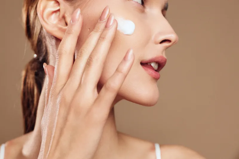 Young woman applies moisturizing cream on her clean face with fingers closeup, skin care routine, natural makeup, beauty treatment, healthy glowing complexion