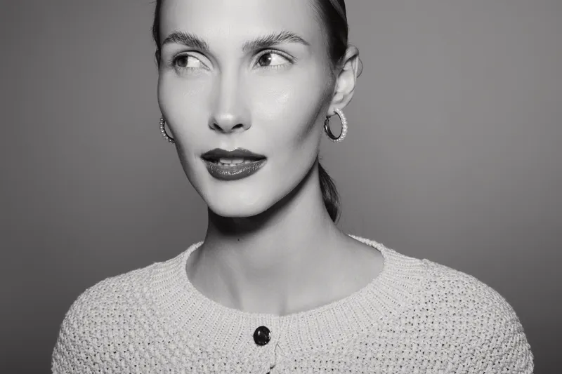 Portrait of a young white woman with fair skin and dark lipstick looking sideways. Studio shot in black and white with soft lighting. Concept of beauty and fashion.