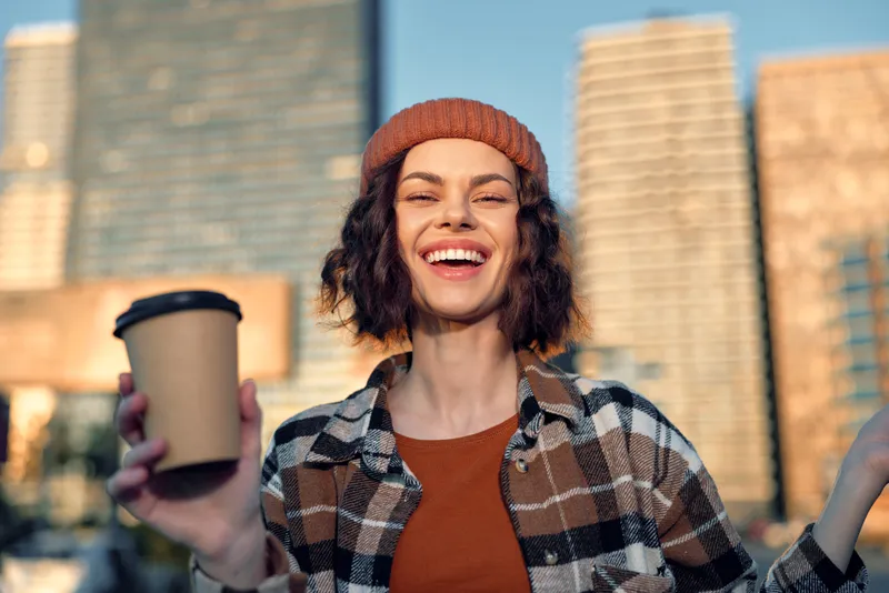 Woman coffee smile city golden candid lifestyle beanie portrait of a joyful young woman holding a coffee cup at golden hour, authentic emotional storytelling and mindful living vibe.
