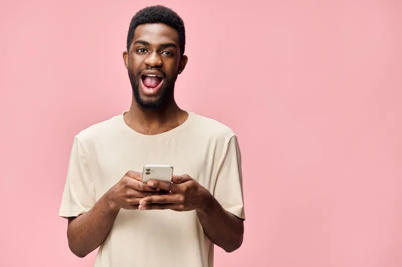 Smiling young man using smartphone on pink background, showcasing happiness and modern lifestyle, perfect for social media and technology themes