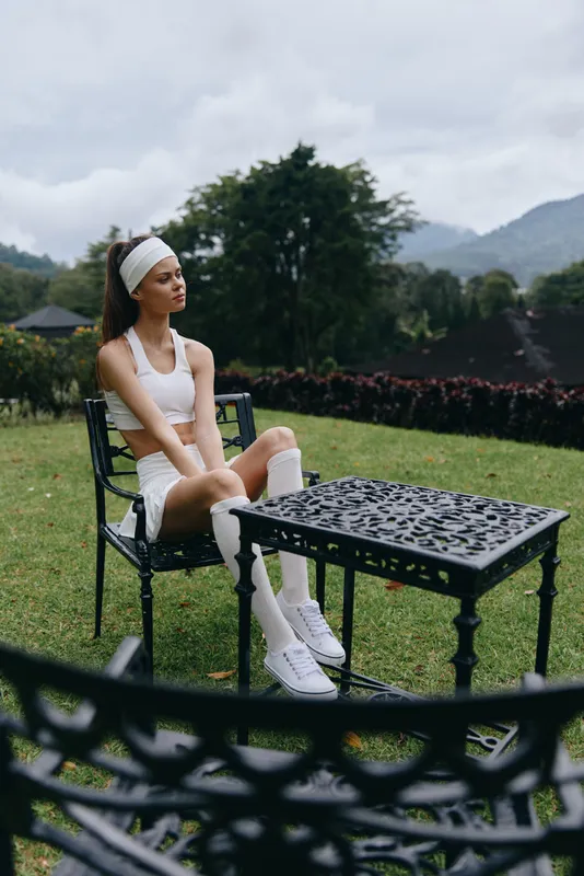 Fit young woman in sporty attire sitting on a chair in a garden, reflecting on a cloudy day, showcasing a healthy lifestyle and outdoor relaxation