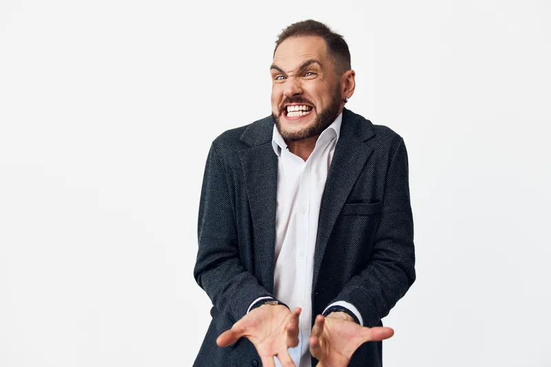 A professional businessman on an isolated color background shows intense emotion. The poised figure exudes energy and focus, with bold gestures and a determined expression, signaling leadership and