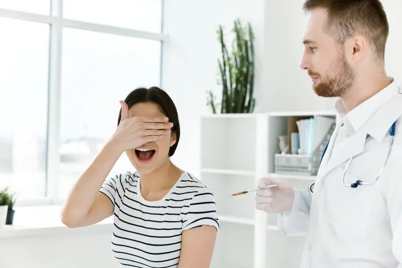 Женщина закрывает глаза рукой во время укола вакцины в больнице