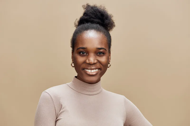 Smiling African woman in beige turtleneck, against a warm brown background, showcasing confidence and elegance, ideal for beauty and fashion themes