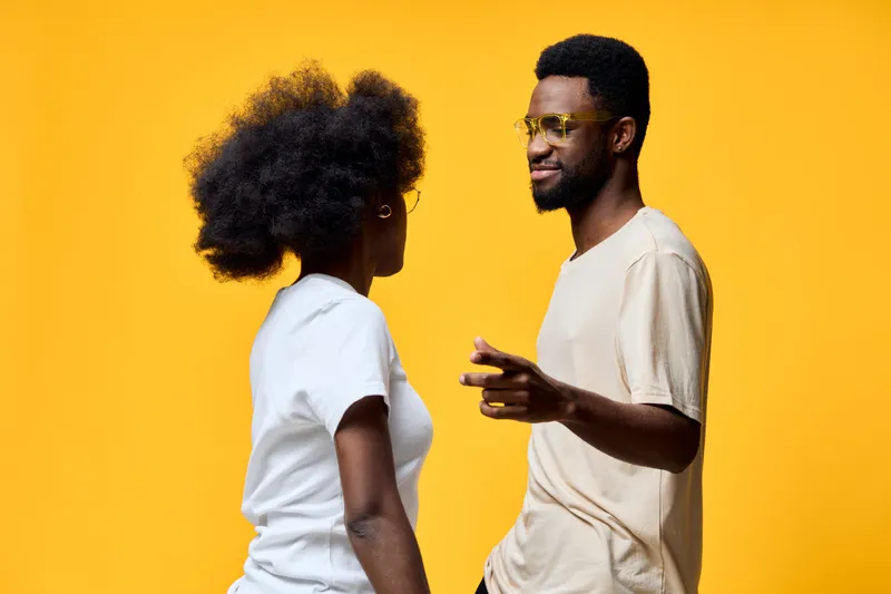 Young diverse couple engaging in conversation against a vibrant yellow background, embodying joy and connection through fashion and emotions