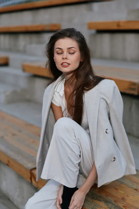 young caucasian woman in stylish light gray business suit sitting outdoors with contemplative expression in urban environment fashion business concept