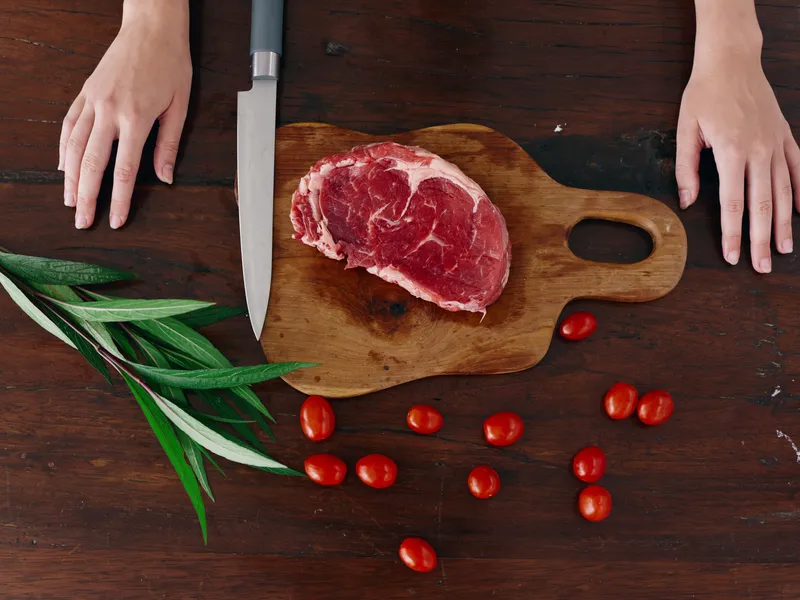 Женщина с ножом в руке нарезает свежее мясо стейка для жарки на кухне