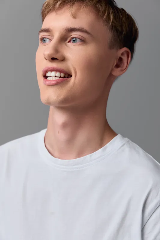 Smiling male with a casual white shirt in a closeup on a gray studio background, expressing happiness, confidence, and positive energy