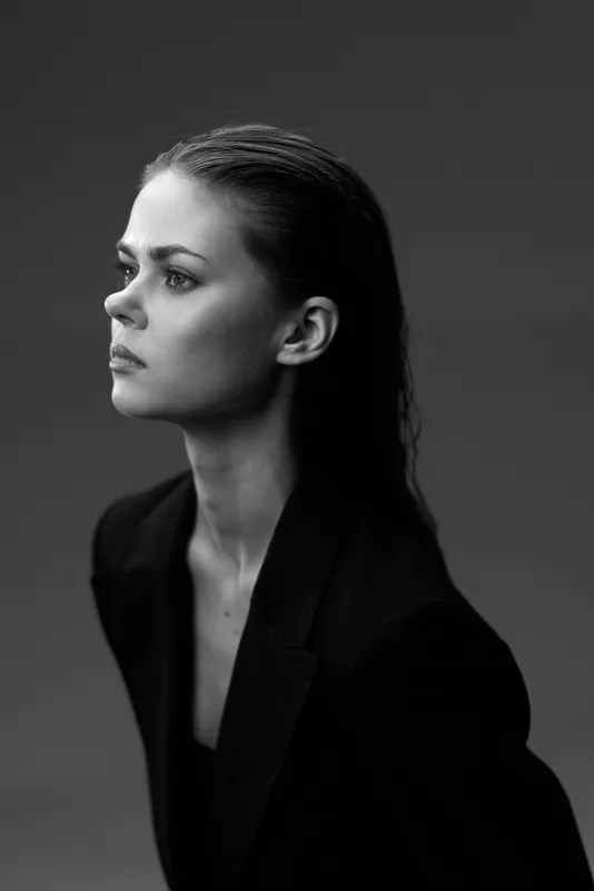 serious woman in black coat looking sideways, black and white portrait with moody lighting