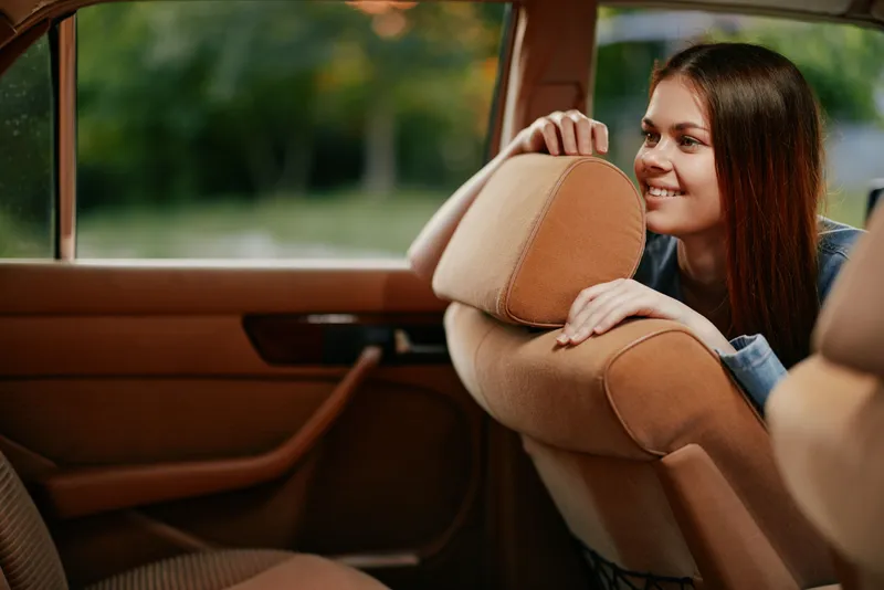 Smiling young woman in a car with a warm brown interior, enjoying a moment of joy and relaxation in nature.