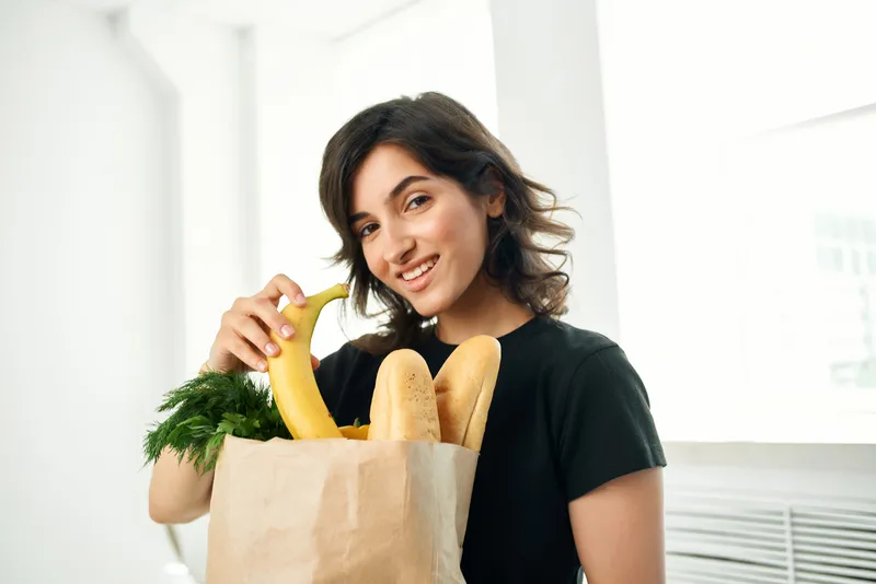 Брюнетка с пакетом продуктов готовит здоровую еду, доставка еды