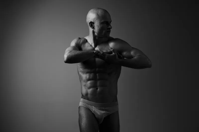 Black and white image of a muscular man posing confidently, showcasing his well-defined physique and strength. A powerful visual representation of fitness and determination.