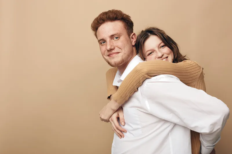 Happy young couple in casual clothes smiling and embracing each other on beige background. Concept of love, friendship, relationship, and positive emotions between people.
