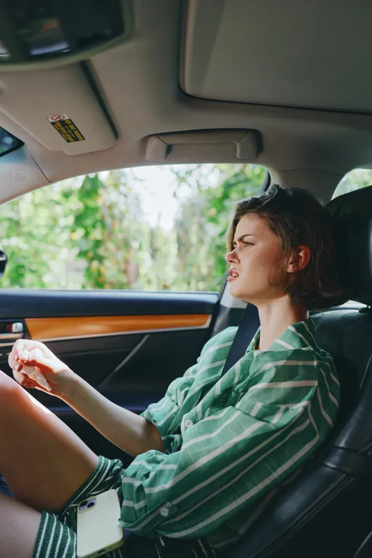 A woman driving a car with a calm expression, seated in the driver seat, hands on the wheel, wearing a green striped shirt.