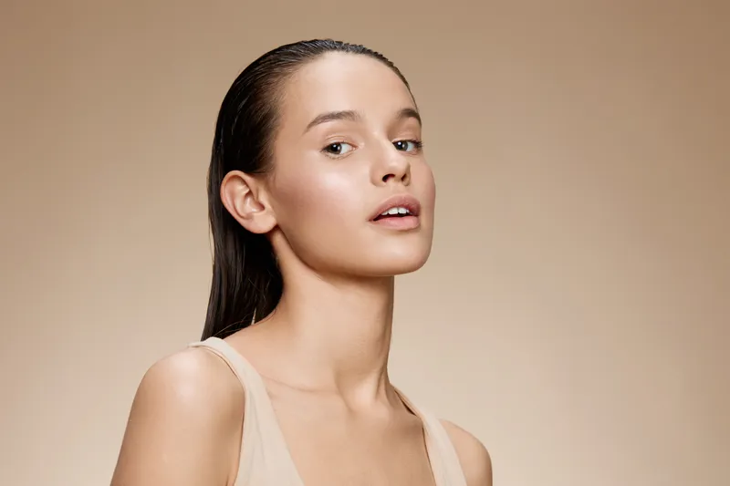Portrait of a young model with an elegant expression, showcasing natural beauty, healthy skin, and minimal makeup against a soft beige background