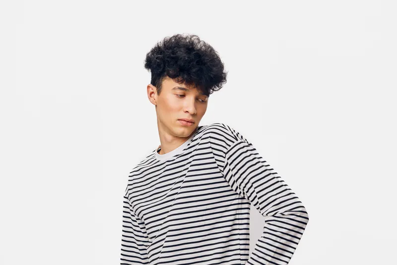 young man with curly hair wearing striped long sleeve shirt looking down thoughtfully, isolated white background, casual style, natural expression