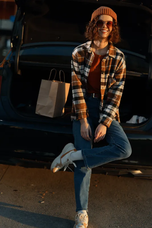 Woman car shopping autumn smile trunk casual sunset posing by open boot, candid lifestyle portrait conveying authenticity, mindful living, golden hour glow and emotional storytelling