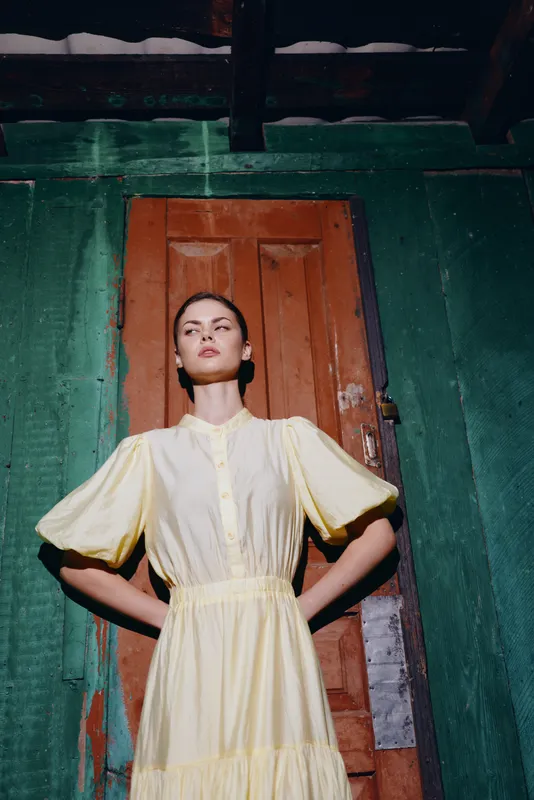 woman portrait dress door vintage confident inclusivity authenticity, female model in yellow dress with hands on hips against rustic wooden door and green wall in dramatic light