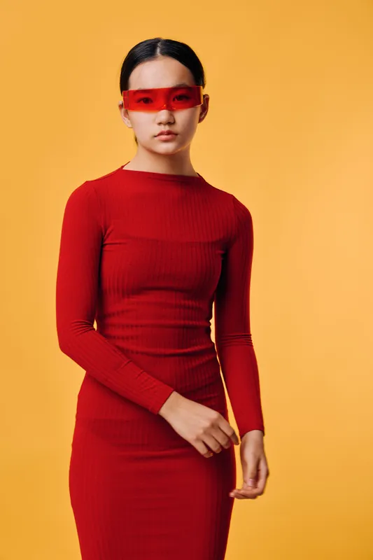 Woman in red dress and futuristic red sunglasses standing against yellow background, fashion style, minimalism, modern, confident pose, studio portrait with clean look and contrast