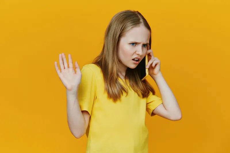 Angry girl talking on the phone with a yellow background, expressing frustration, casual wear, capturing emotion in a vibrant and youthful style