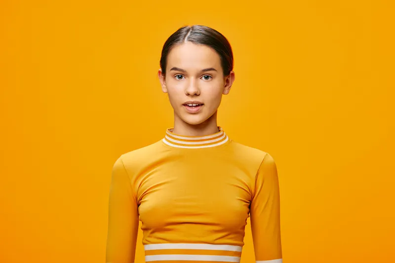 Female fitness model in a bright yellow athletic top stands against a solid yellow backdrop, conveying sport, health, and active lifestyle with focus on fitness apparel.