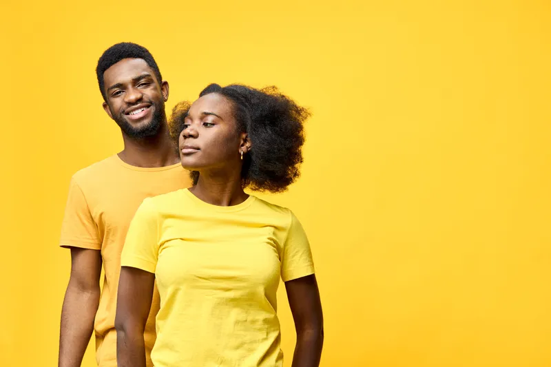 A joyful young African couple wearing matching yellow t shirts, standing against a bright yellow background, showcasing love and connection in a vibrant, cheerful setting