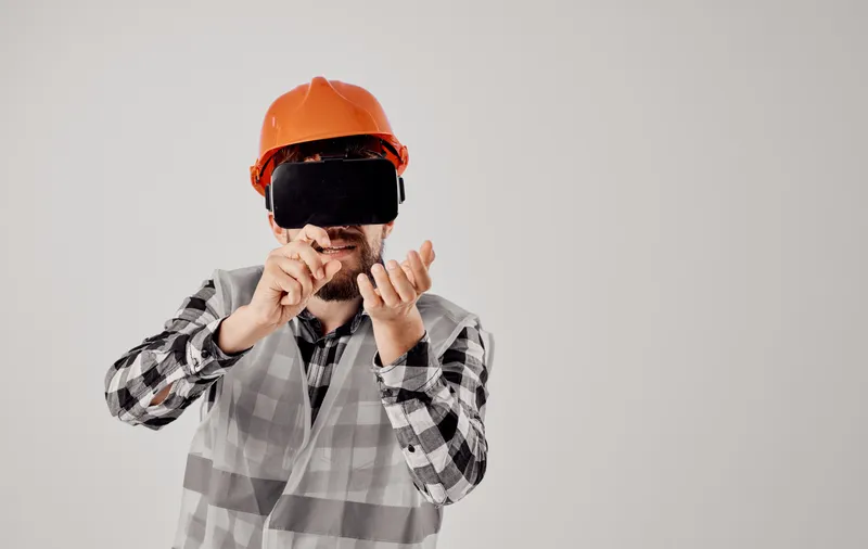 Строитель в оранжевой каске и 3D-очках жестикулирует руками, свободное пространство, светлый фон