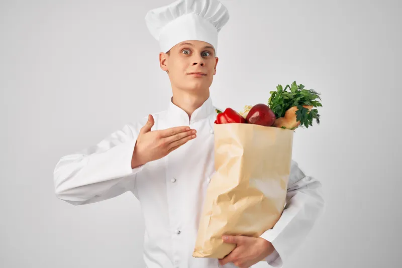 Мужчина в униформе шеф-повара держит упаковку с продуктами, готовит и работает в ресторане