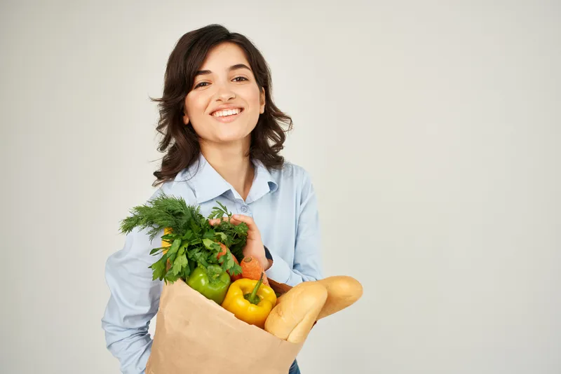 Брюнетка с пакетом продуктов из супермаркета: здоровая еда, овощи