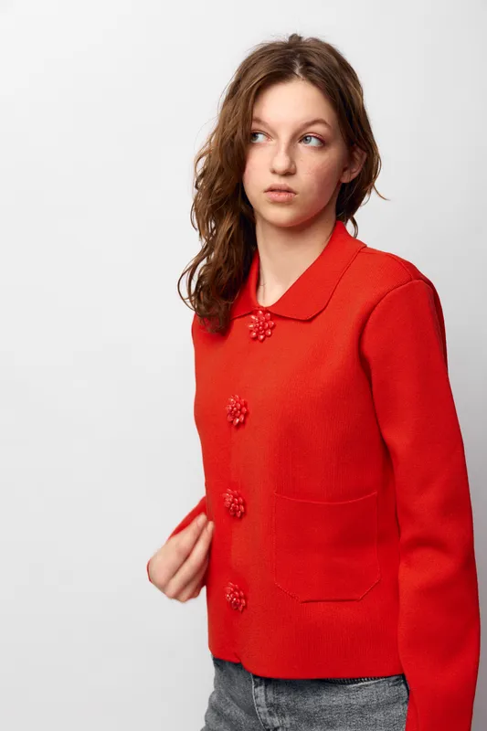 Young woman with long brown hair wearing a red knitted sweater looks to the side with a thoughtful expression. Casual fashion concept with bright clothing and natural pose on white background.
