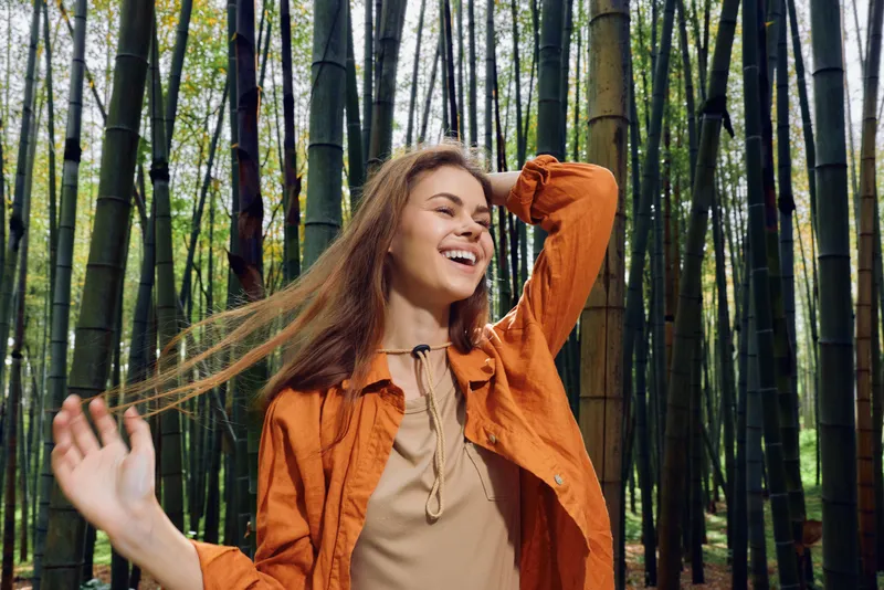Woman smile bamboo forest portrait nature joy outdoors, young woman in orange shirt laughing with eyes closed among tall bamboo stalks, carefree motion, lifestyle, travel and wellness.