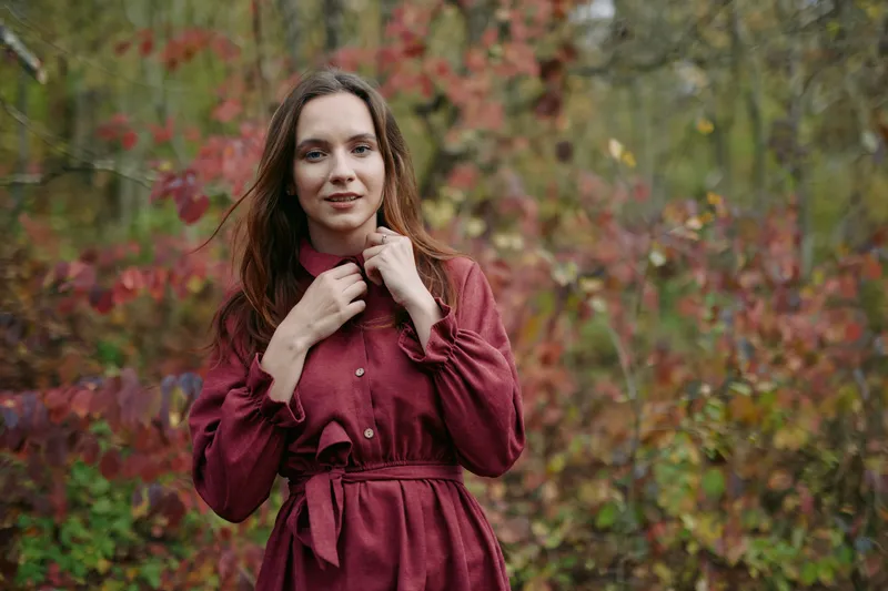An authentic portrait of a young woman in a burgundy dress amid autumn foliage, presenting sincere mood and credibility through natural pose and gentle gaze that conveys trust and honesty for