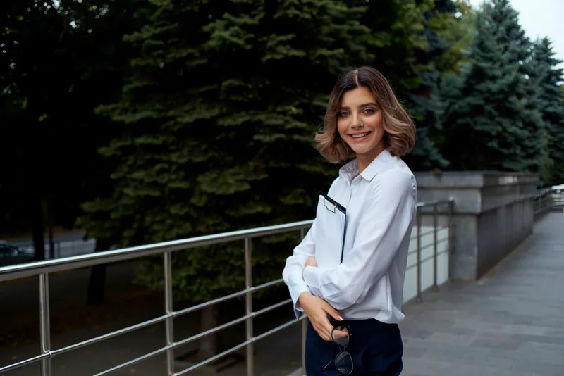 Женщина на улице держит в руках документы, она выглядит как менеджер