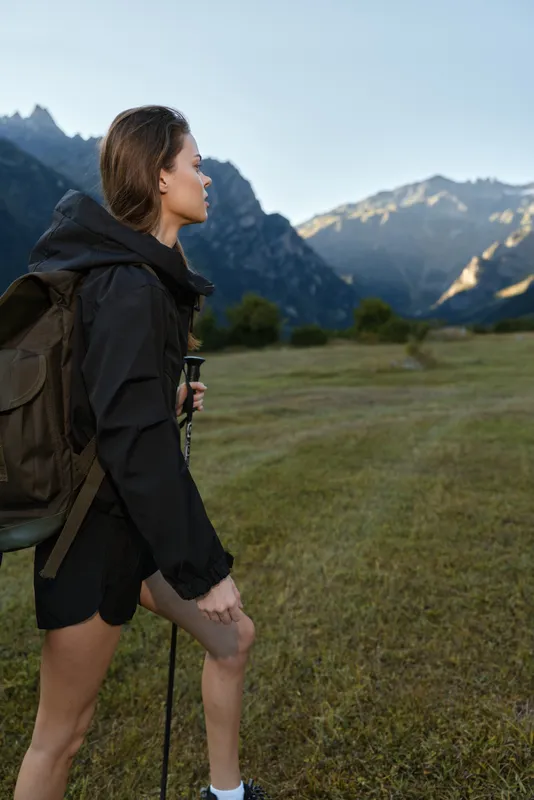 A young female hiker with a sturdy backpack walks through a grassy valley toward rugged mountains. She looks focused, adventurous, and ready for outdoor exploration.