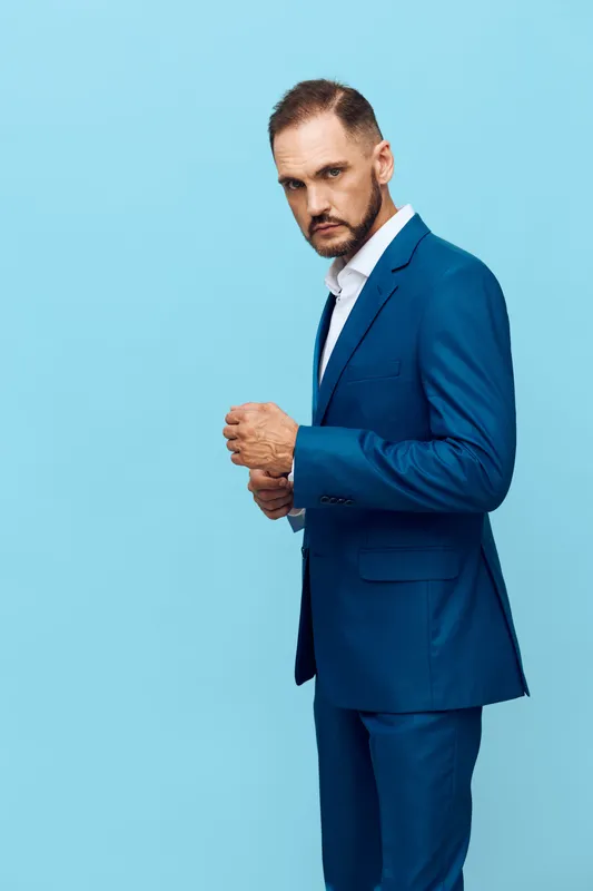 A professional business man stands against a solid blue background, conveying confidence and focus, an isolated color backdrop perfect for corporate or leadership themes.