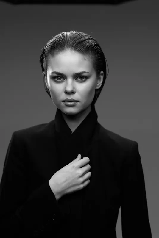 Black and white portrait of a serious woman with slicked-back hair wearing dark clothing, showing strength and confidence.