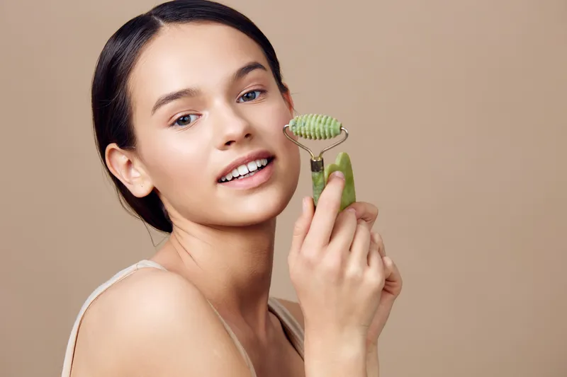 Young woman applying a jade roller for skincare, showcasing natural beauty and wellness, with a soft, neutral background that emphasizes relaxation and self care