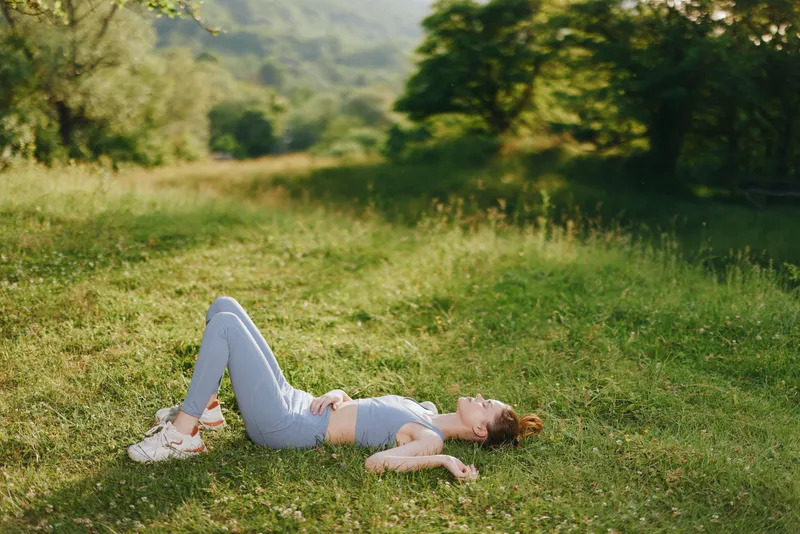 Energetic young woman practicing yoga outdoors in a serene green field, wearing a matching light blue outfit, conveying relaxation and mindfulness through her pose