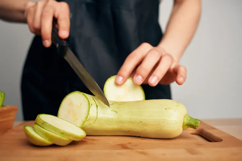 Женщина в черном фартуке нарезает овощи на кухне, готовит еду